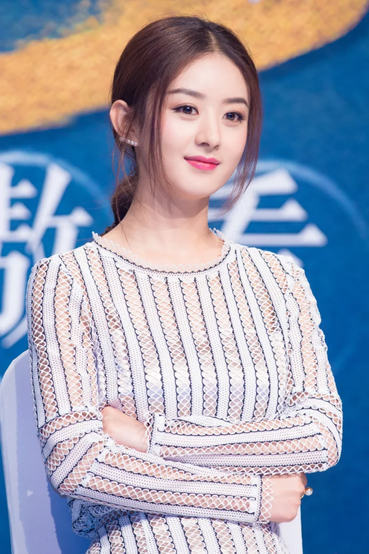 一名成年女性穿着浅色纹理针织衫，在蓝色背景前交叉双臂。