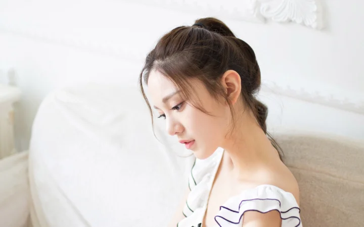 一名成年女性在明亮的白色室内侧身低头而坐。