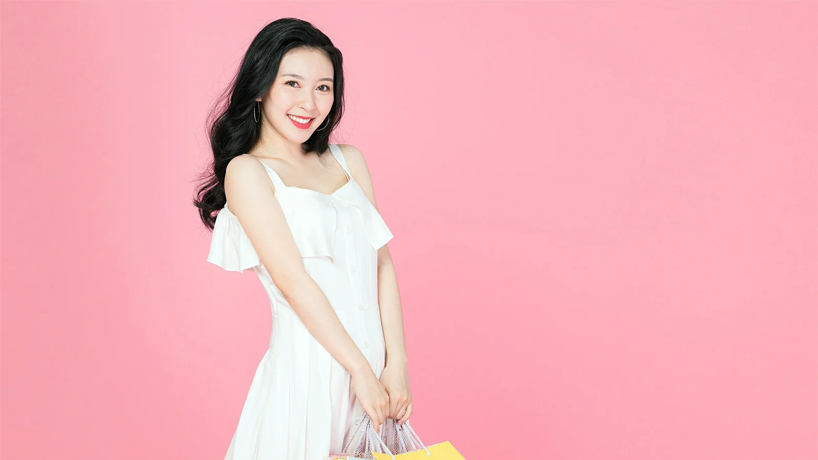 흰색 원피스를 입은 성인 여성이 분홍색 배경 앞에서 미소 짓고 있다.