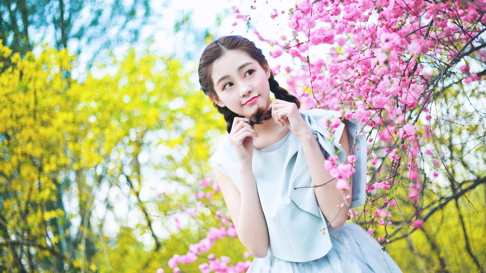 一名年轻女性站在粉色花树旁，周围是明亮的春日树木。