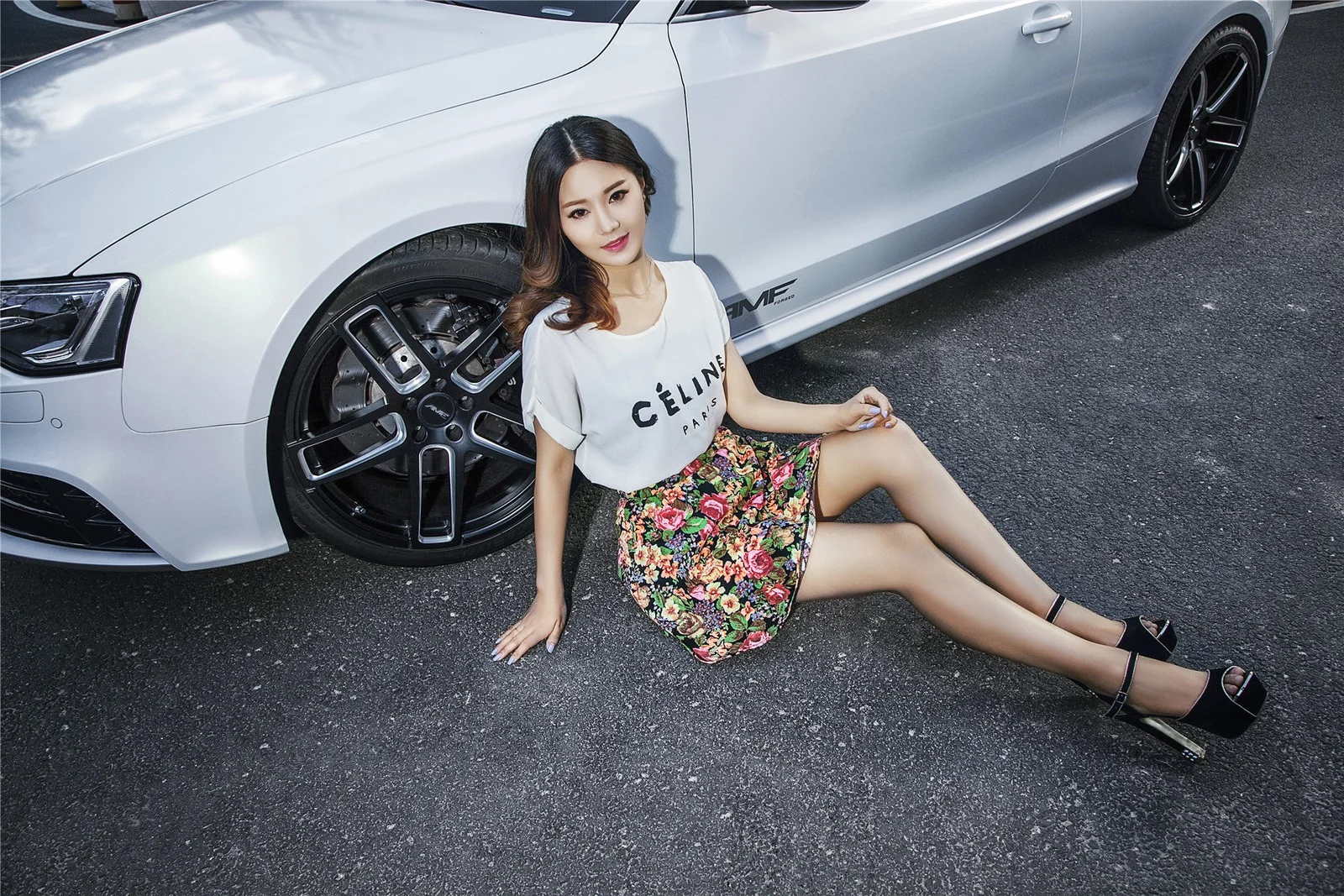 一名女性坐在白色汽车旁的地面上。