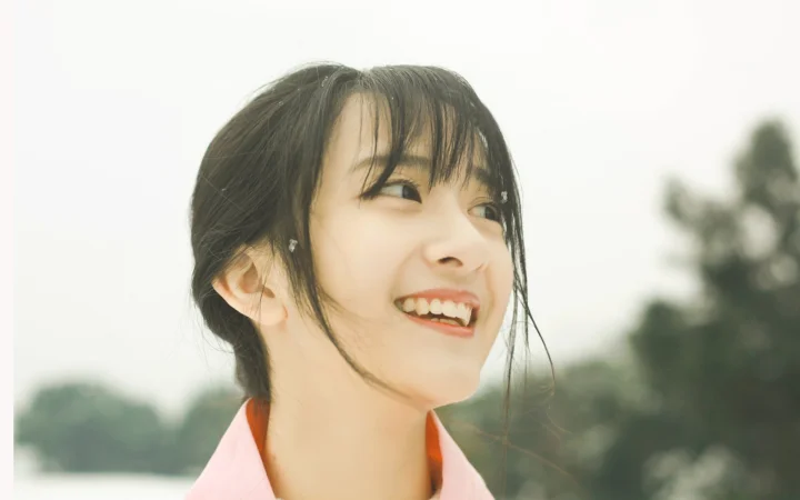 若い女性が屋外の背景を前に横を向いて微笑んでいる。