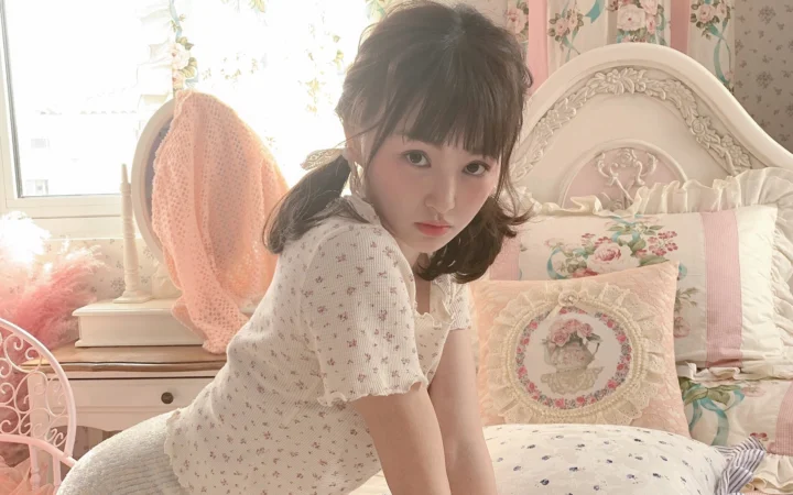 꽃무늬 장식과 침구가 있는 침실에서 여성이 카메라를 바라보고 있다.