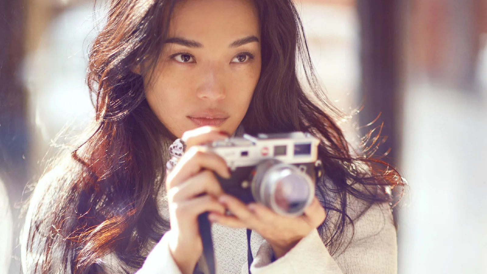 成人女性がレトロなカメラを手に、柔らかな光の中でこちらを見つめています。