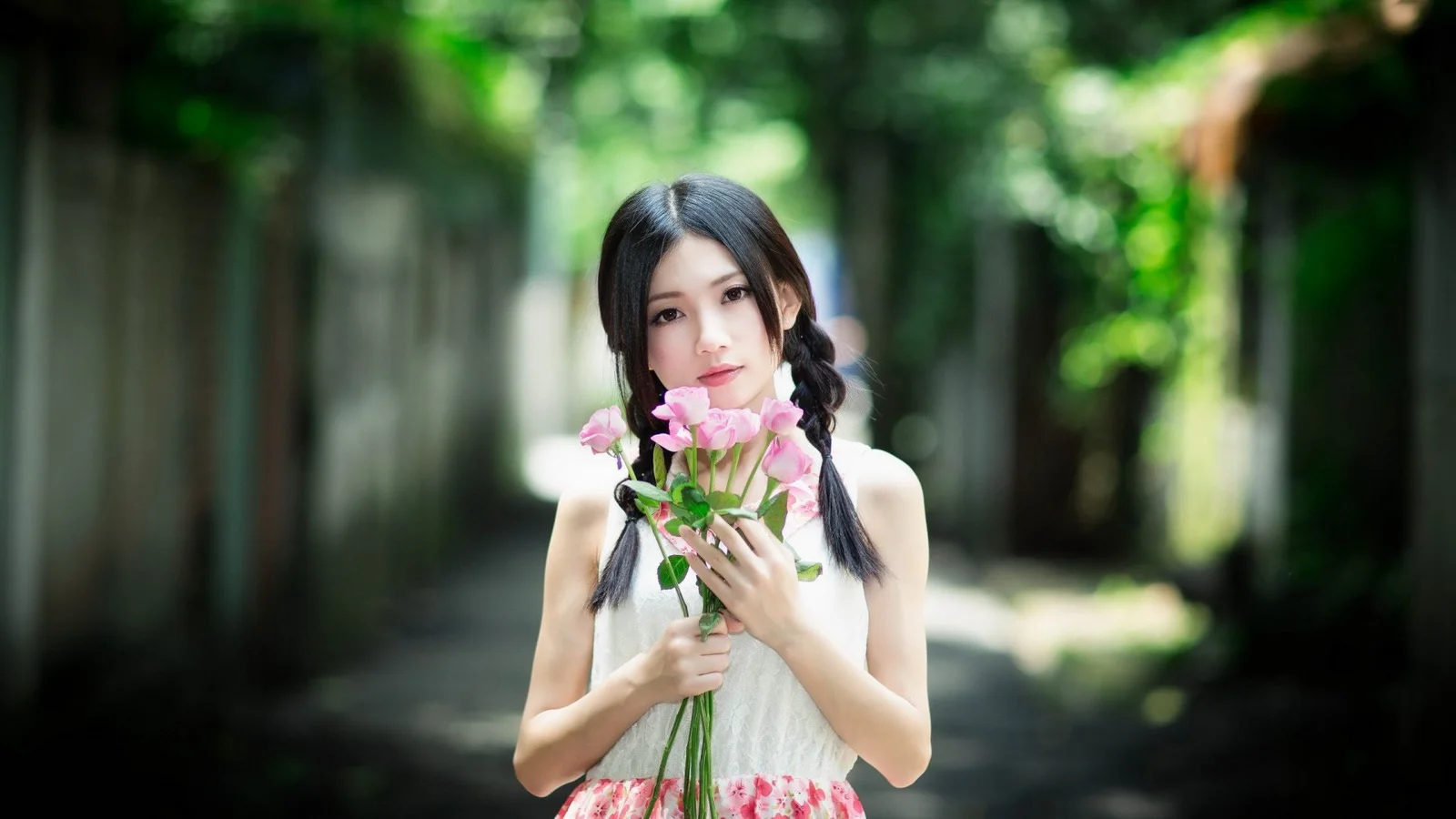 一名女子站在林间小路上，手捧一束粉色花朵。