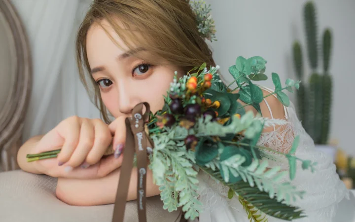 一名成年女性手持花束和剪刀，靠在室内椅背上看向镜头。