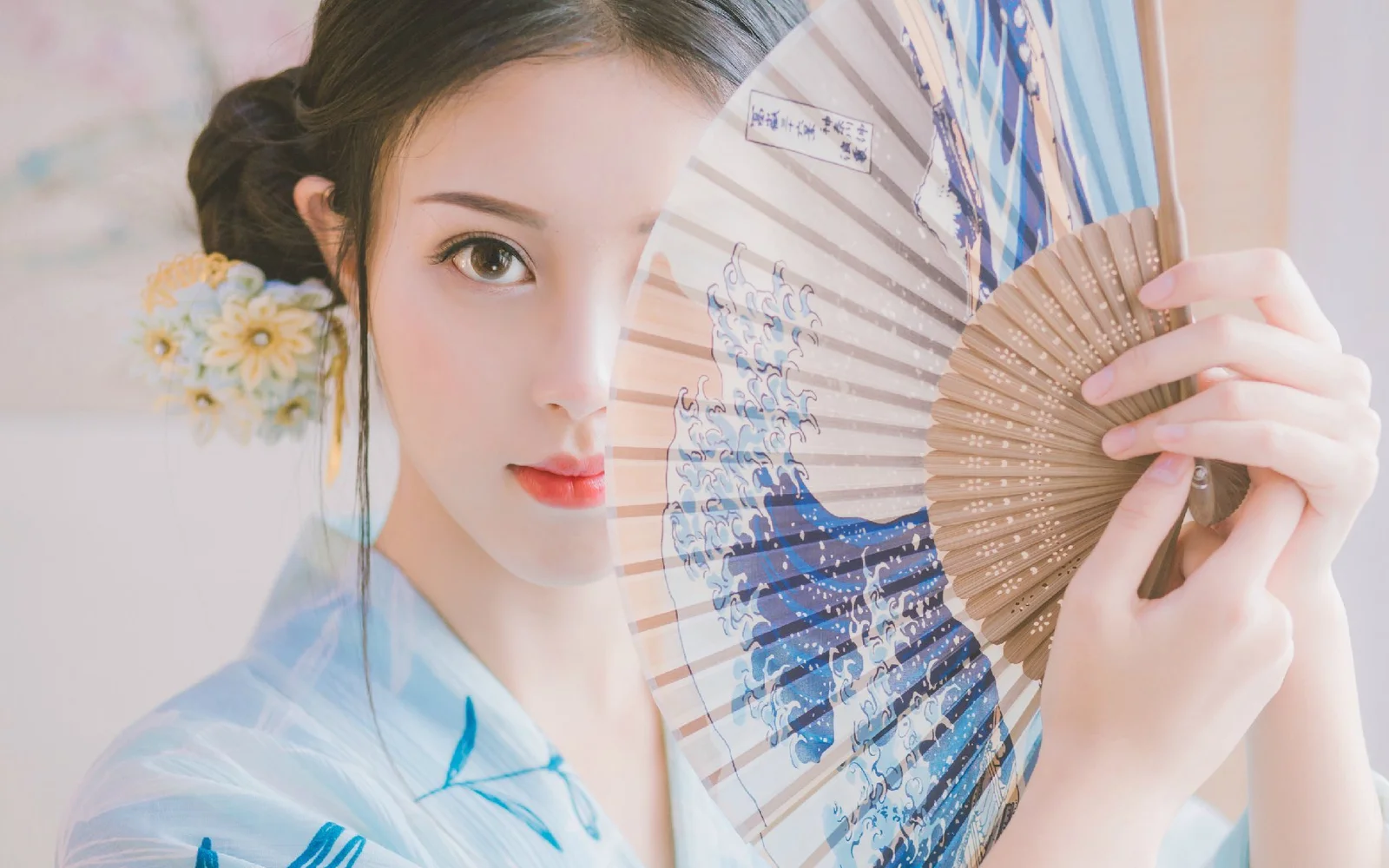 一位成年女子手持折扇面对镜头，画面呈现柔和的古风人像氛围。