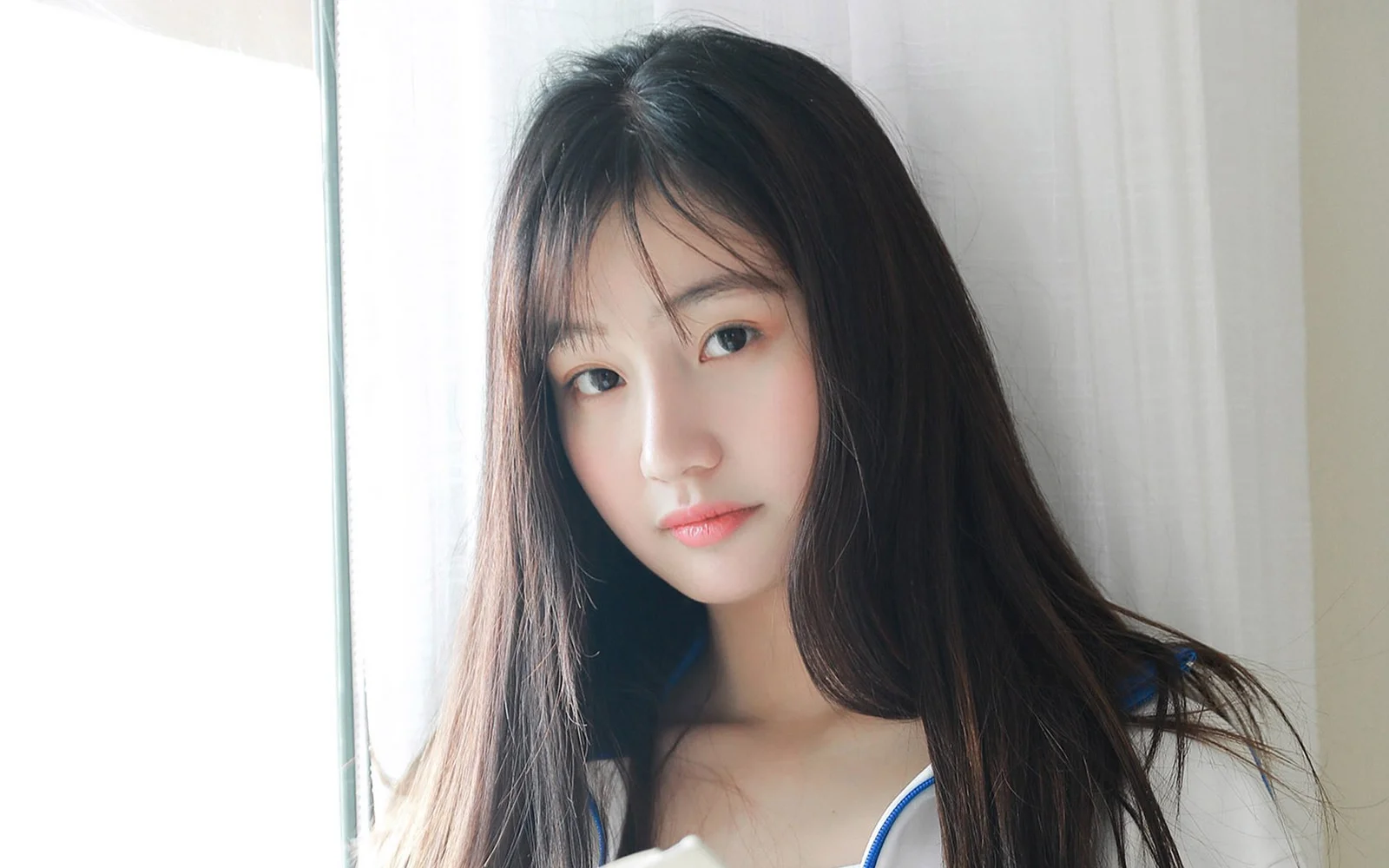 一位长发女性在室内窗边的近距离肖像画面。