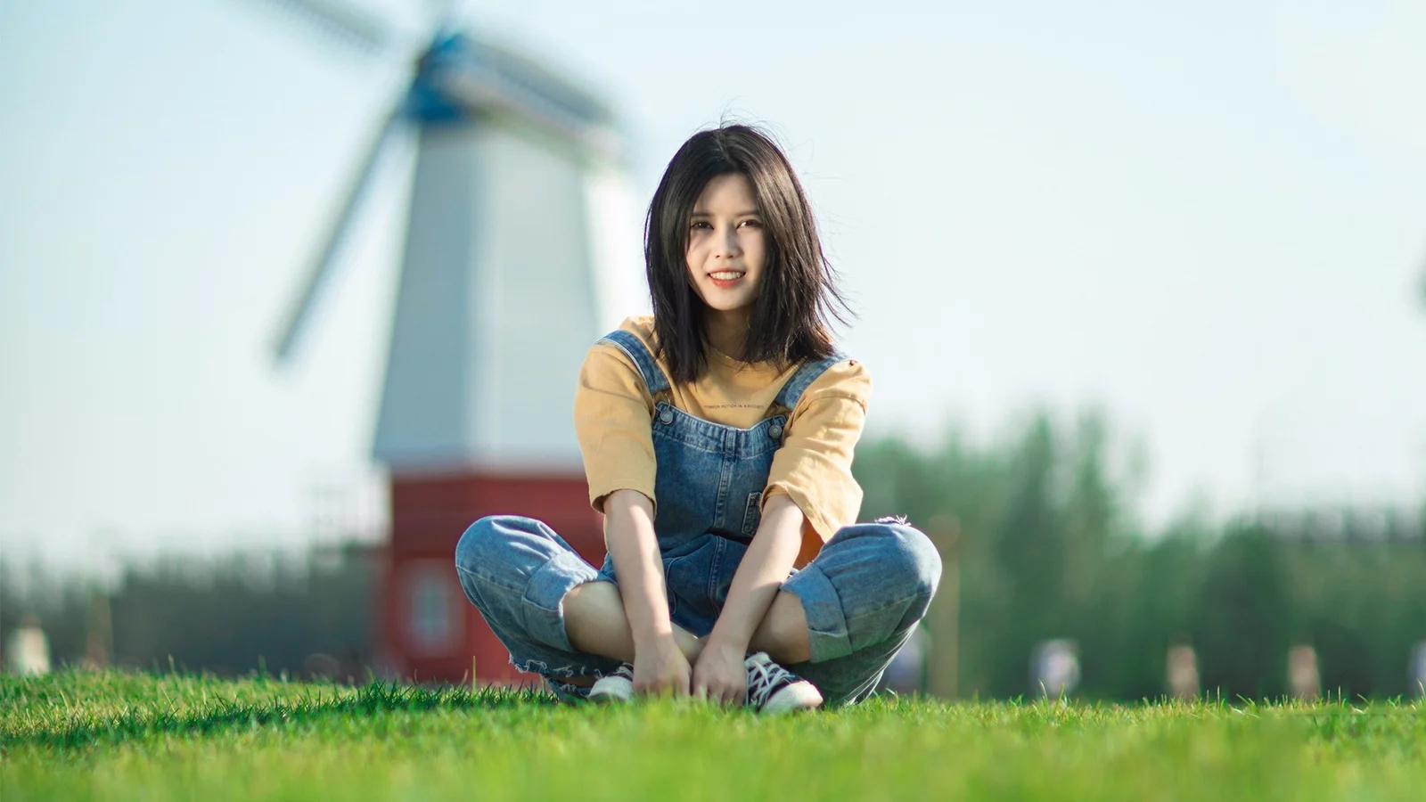 一名女子坐在阳光明媚的草地上，身后是模糊的风车。