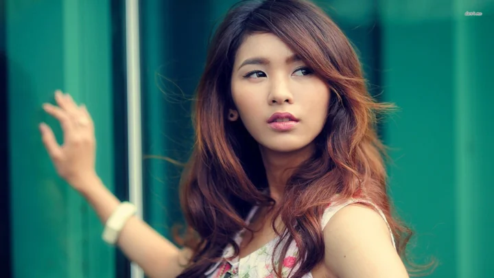 一名长发女性站在绿色玻璃背景前，侧头望向一旁。