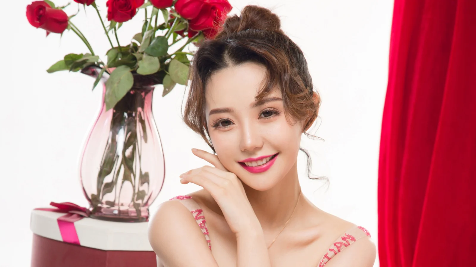 一名成年女性在红玫瑰花瓶和红色窗帘前微笑入镜。