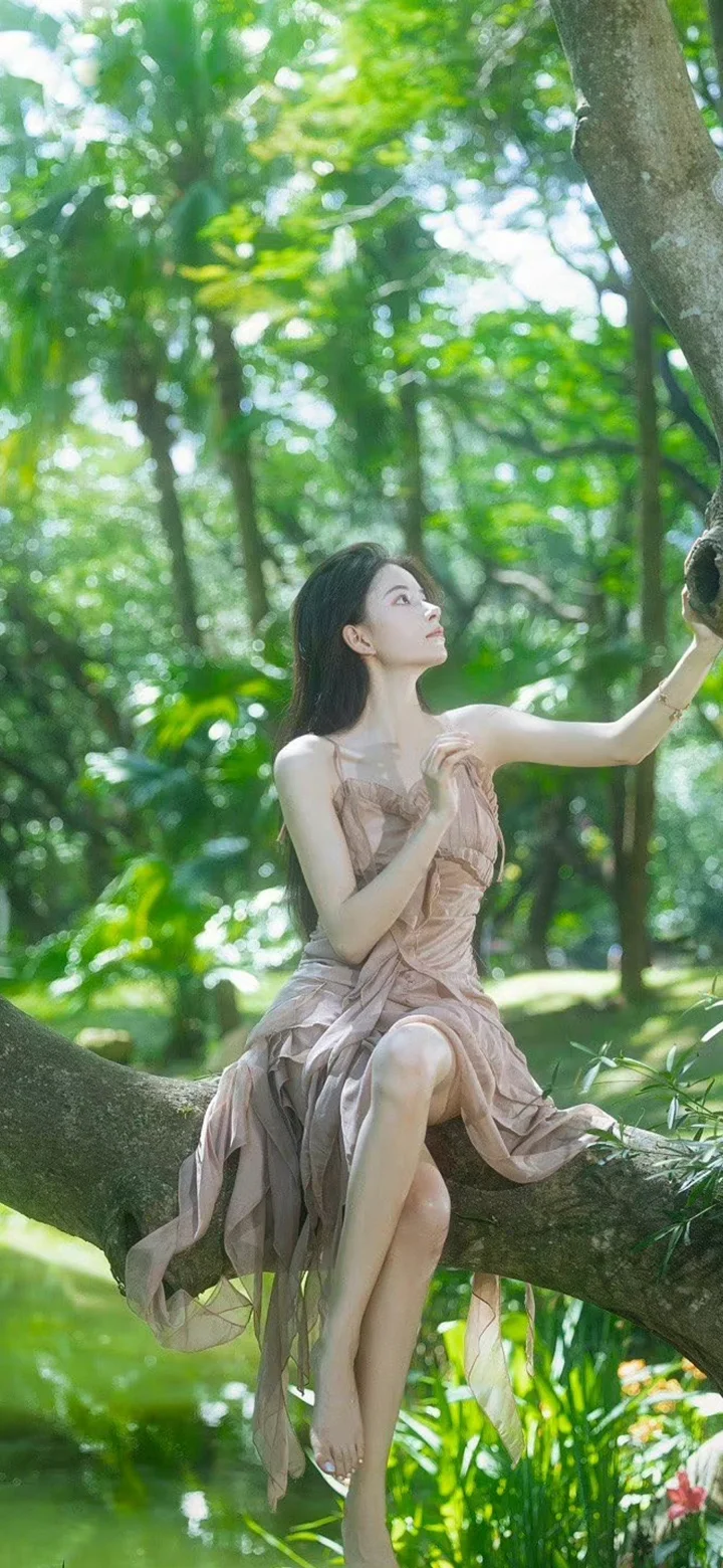 一名身穿浅色连衣裙的成年女子坐在森林树枝上，周围是茂密的绿色树叶。