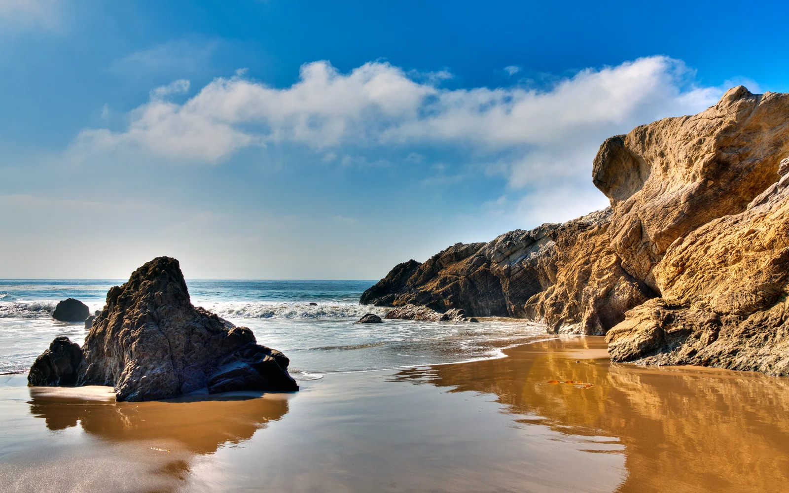 陽光照耀著被礁石環繞的海灘，海水與天空在遠處相接。