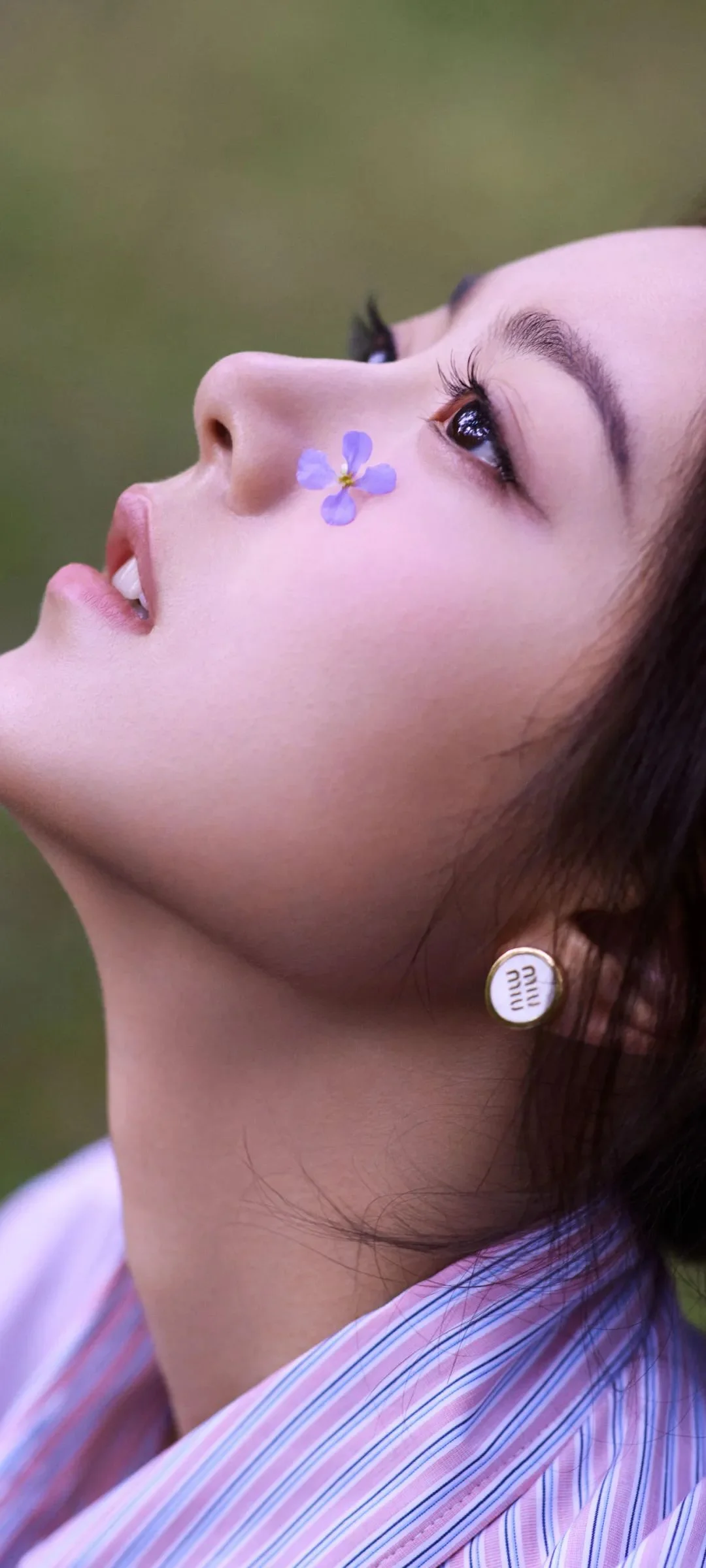 한 여성이 옆얼굴로 위를 바라보며 볼에 작은 보라색 꽃을 붙이고 알록달록한 줄무늬 옷을 입고 있습니다.