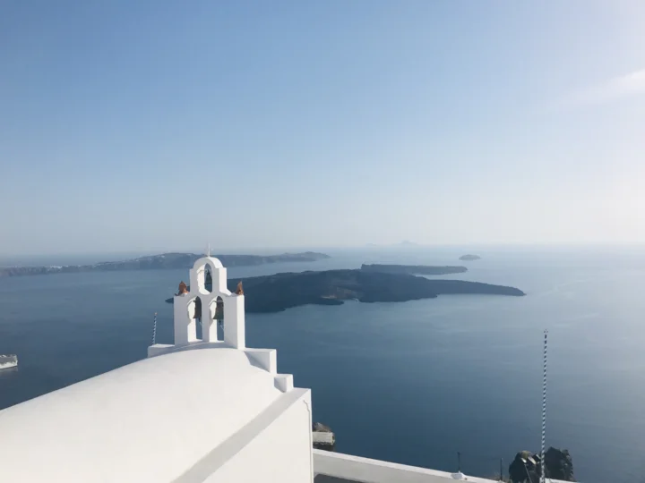 白色教堂坐落在海湾与远处岛屿前方，构成宁静的圣托里尼海景。