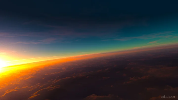 夕阳从云层上方照亮倾斜的地平线，天空呈现深蓝、青绿与橙黄色渐变。