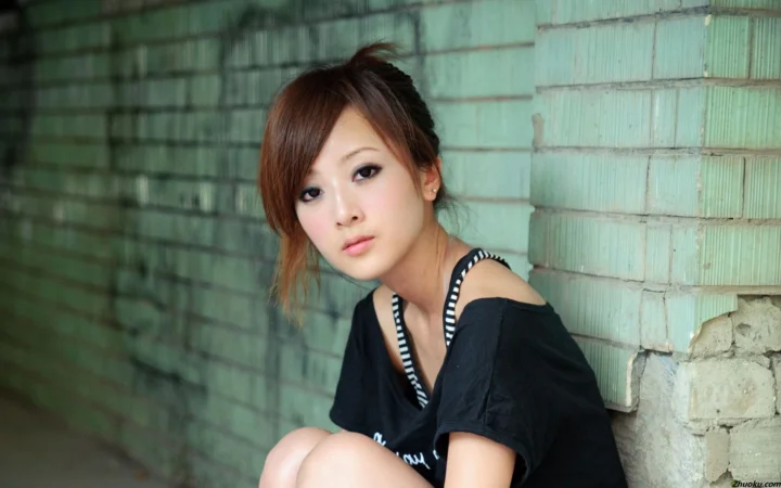 一名女性坐在砖墙旁，面对镜头拍摄肖像。