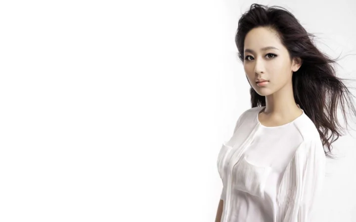 一名长发女性穿着白色上衣站在白色背景前。