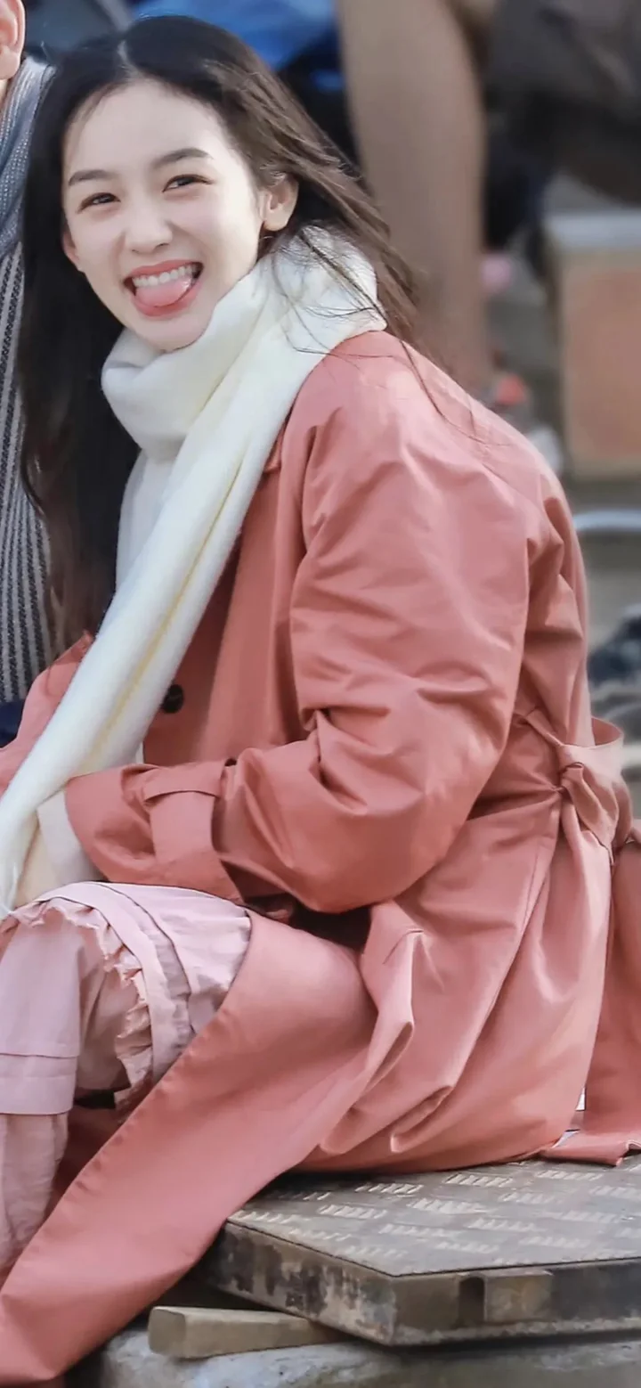 一名微笑的女性穿着粉色外套和浅色围巾坐在户外。