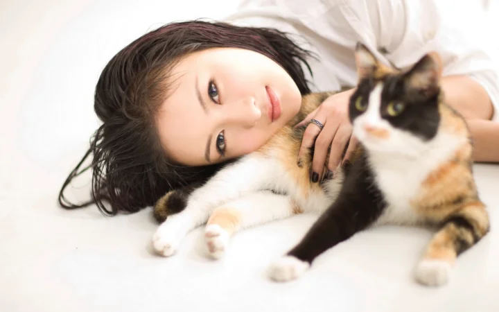 一名女性躺在白色床面上，身旁有两只猫咪。