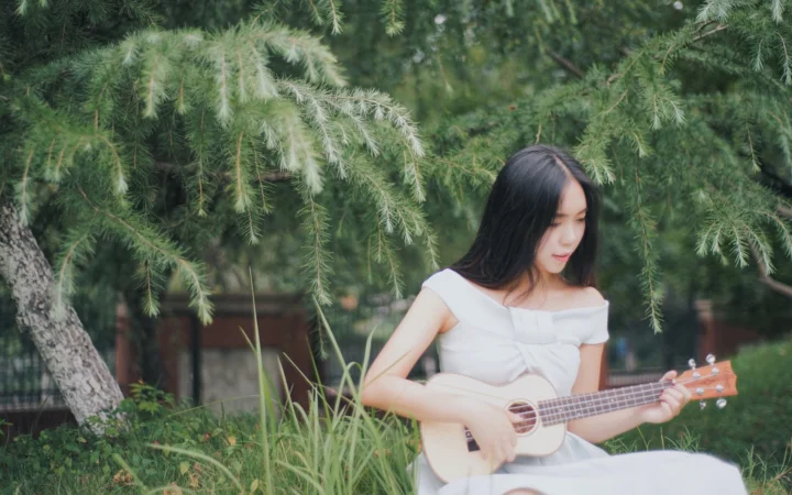 一名女子坐在绿意盎然的户外环境中弹奏尤克里里。