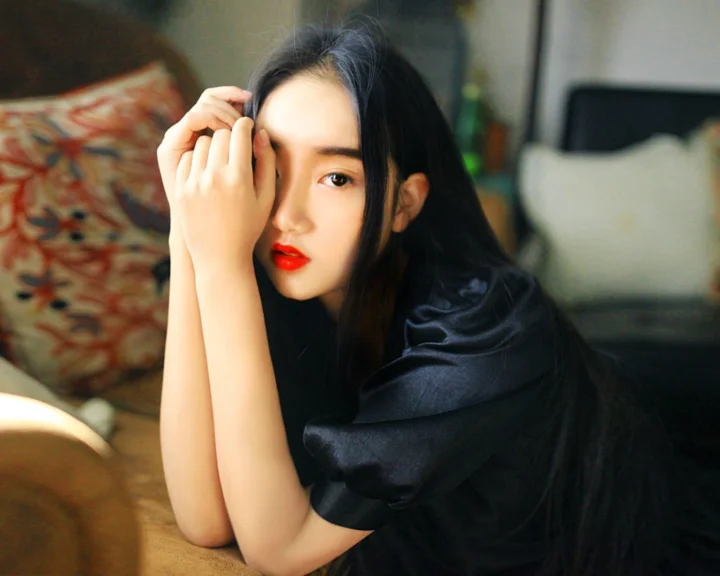 一名黑发女性身穿黑色上衣，靠在桌边直视镜头。