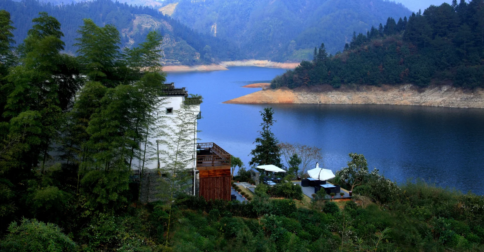 湖水、山林和远处群山构成宁静的黄山自然风景，岸边可见一座建筑。