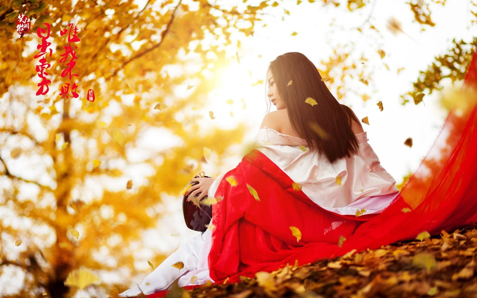 一名女子身穿红色长裙坐在铺满落叶的秋日树林中。