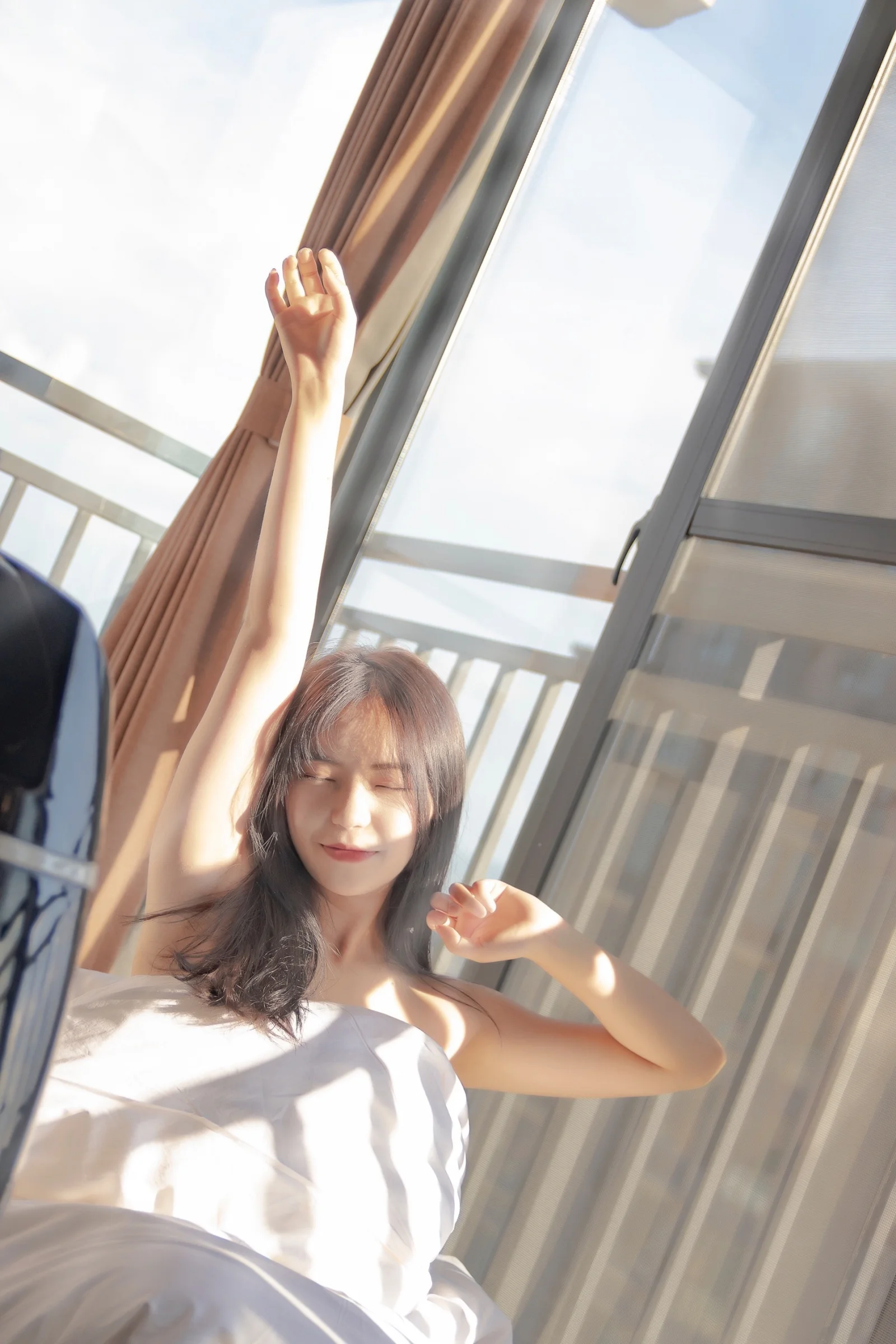 一名女子站在窗边，抬起手臂沐浴在明亮的阳光中。