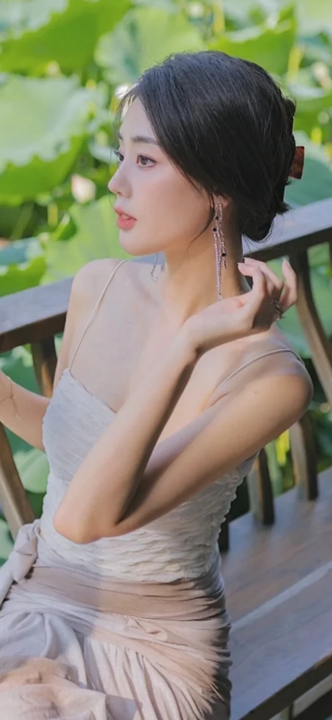 一位穿着浅色连衣裙的女子在荷叶旁侧身整理头发。