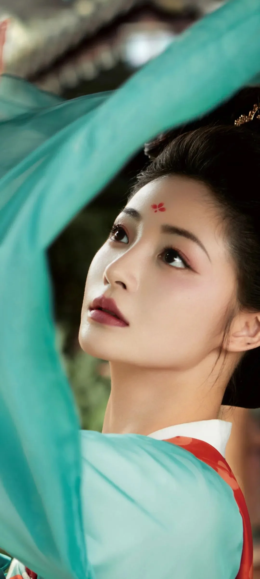연한 녹색 전통 의상을 입은 여성이 위를 바라보는 얼굴 중심의 클로즈업입니다.