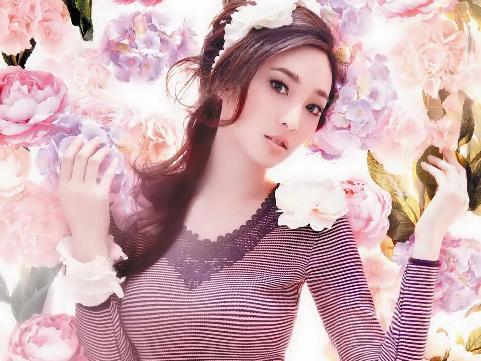 一名长发女子站在粉色和紫色花朵之间，面向镜头微笑。