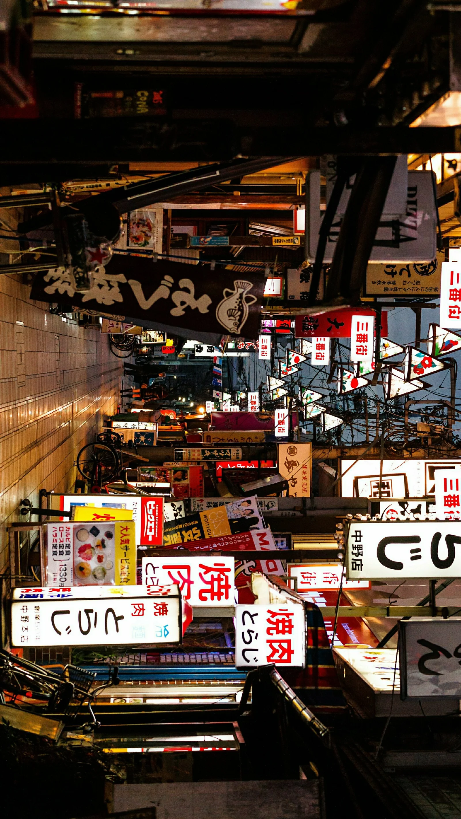 一条狭窄的城市街巷两侧布满店铺、悬挂招牌和明亮的广告牌。