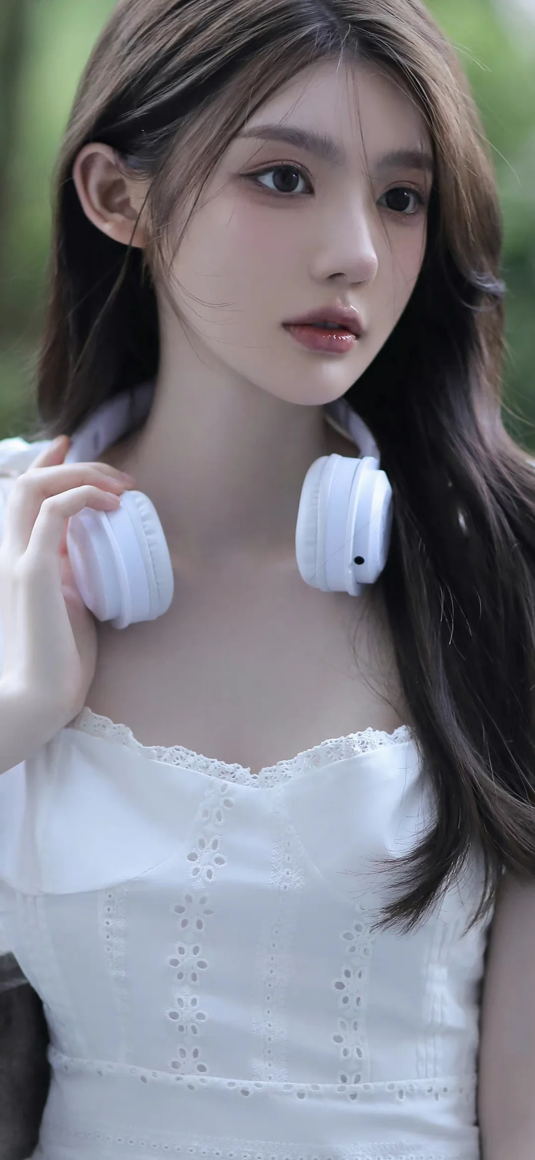 一位長髮女性戴著白色耳機，身穿白色上衣站在綠色背景前。