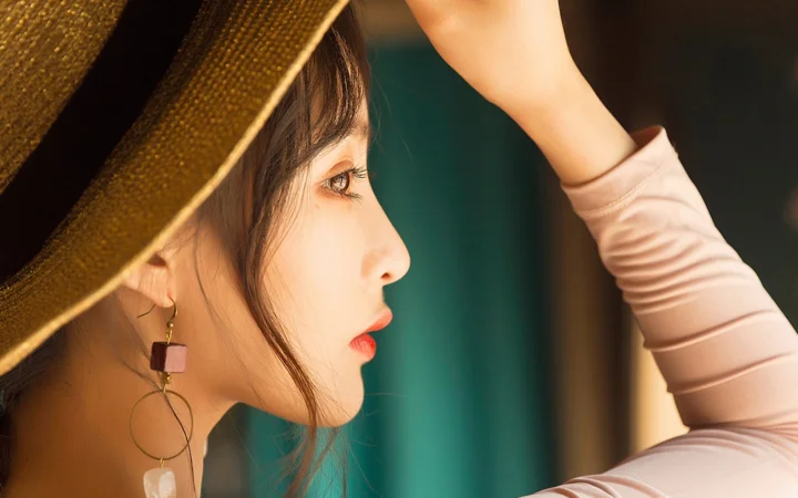 챙이 넓은 모자를 쓴 성인 여성이 한쪽 팔을 올린 채 오른쪽을 바라보는 옆모습으로 담겨 있습니다.