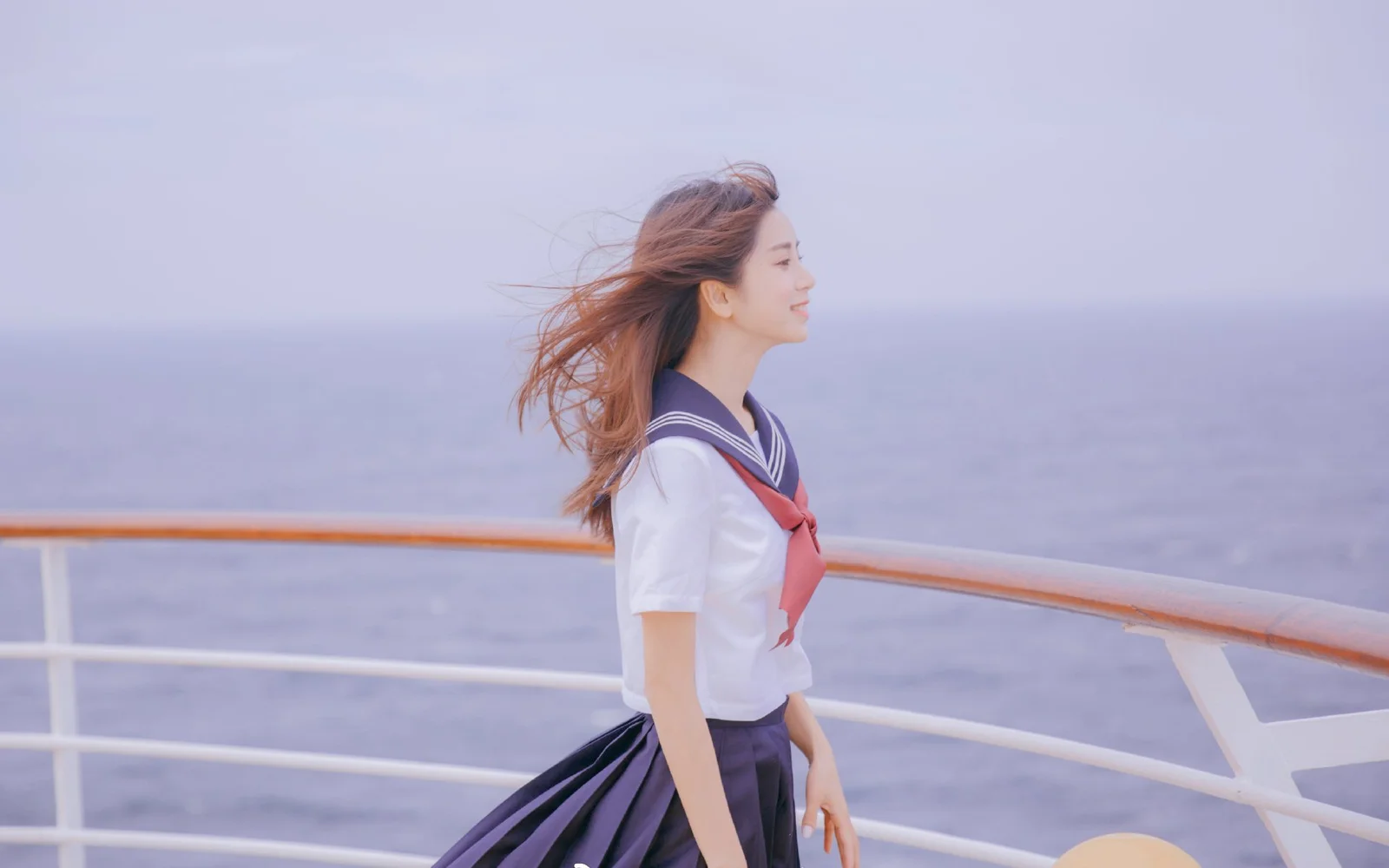 長い髪の女性が船の甲板に立ち、海を眺めている。