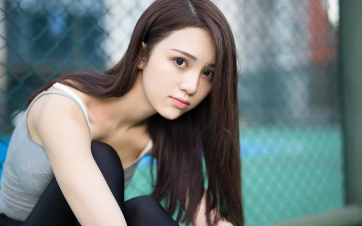 一名长发女性在铁丝网背景前侧身注视镜头。