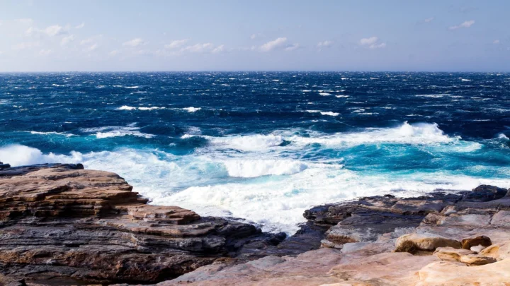 湛蓝海面上的白色海浪不断冲击着岩石海岸。
