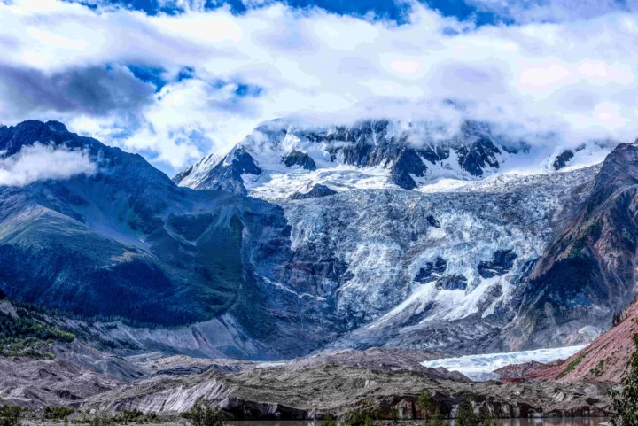 壮丽的雪山冰川在云层下延展开来，前景可见少量湖水。