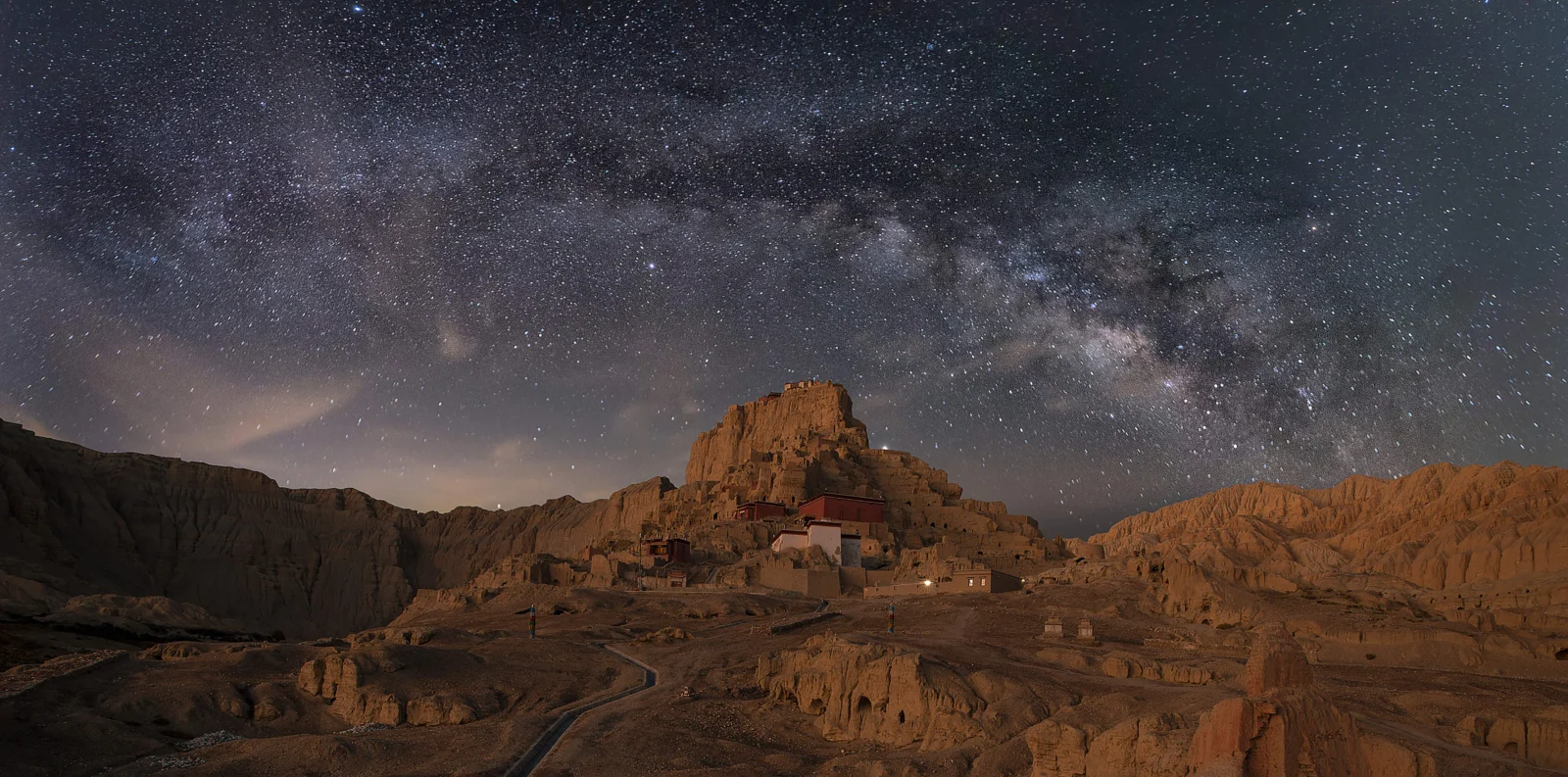 银河横跨星空，照亮了荒凉的群山和山谷中的建筑。