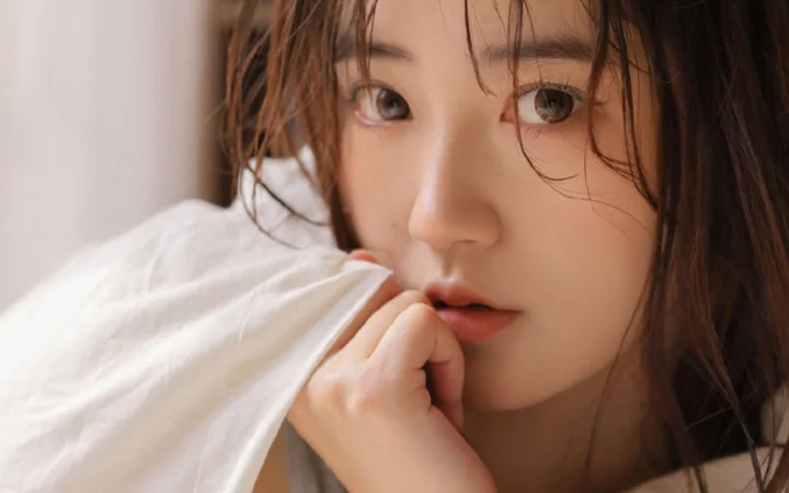 부드러운 빛 속에서 젖은 갈색 머리카락이 얼굴을 감싸고 손가락을 입술에 댄 여성의 클로즈업 인물 사진이다.