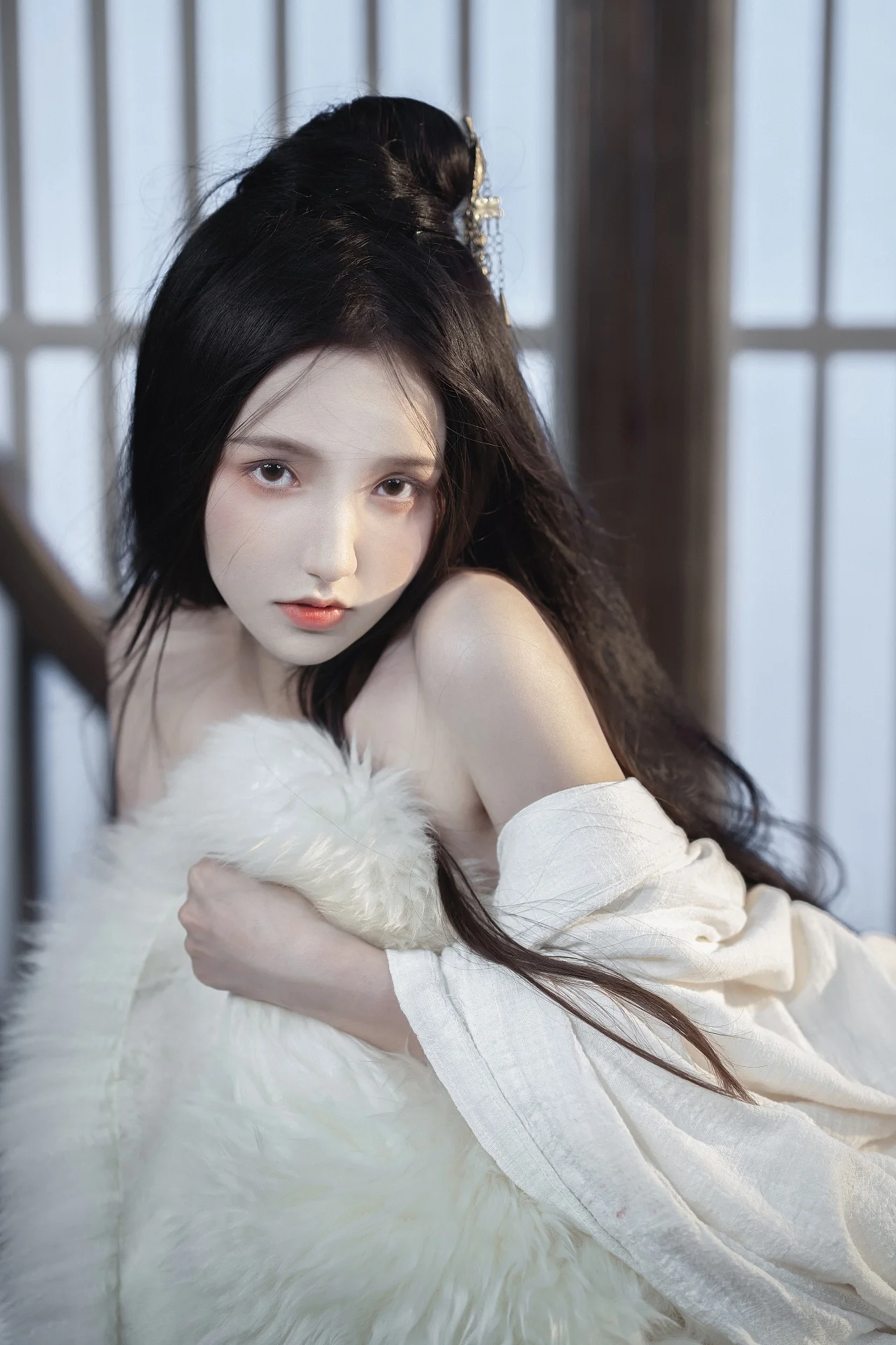 一名長髮女子穿著白色服裝坐在室內窗邊，懷抱白色絨毛靠墊看向鏡頭。