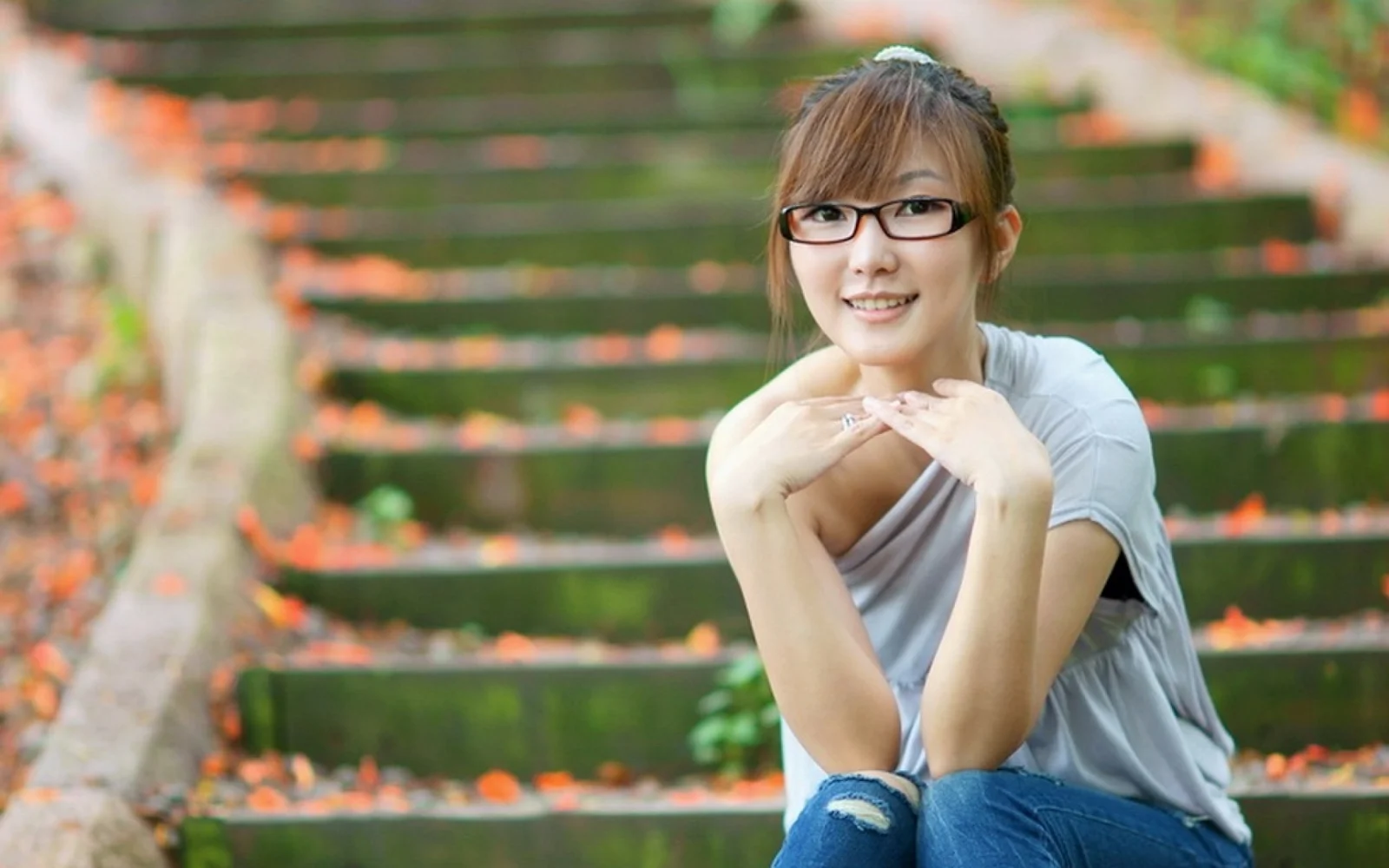 一名戴眼镜的女性坐在户外台阶上微笑面对镜头。