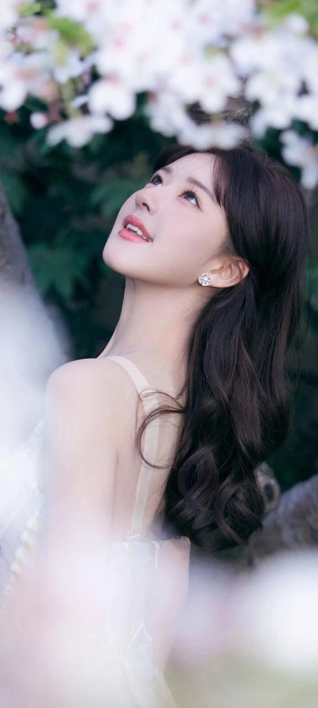 一名长发女子在白色花朵和绿色 foliage 前抬头微笑。