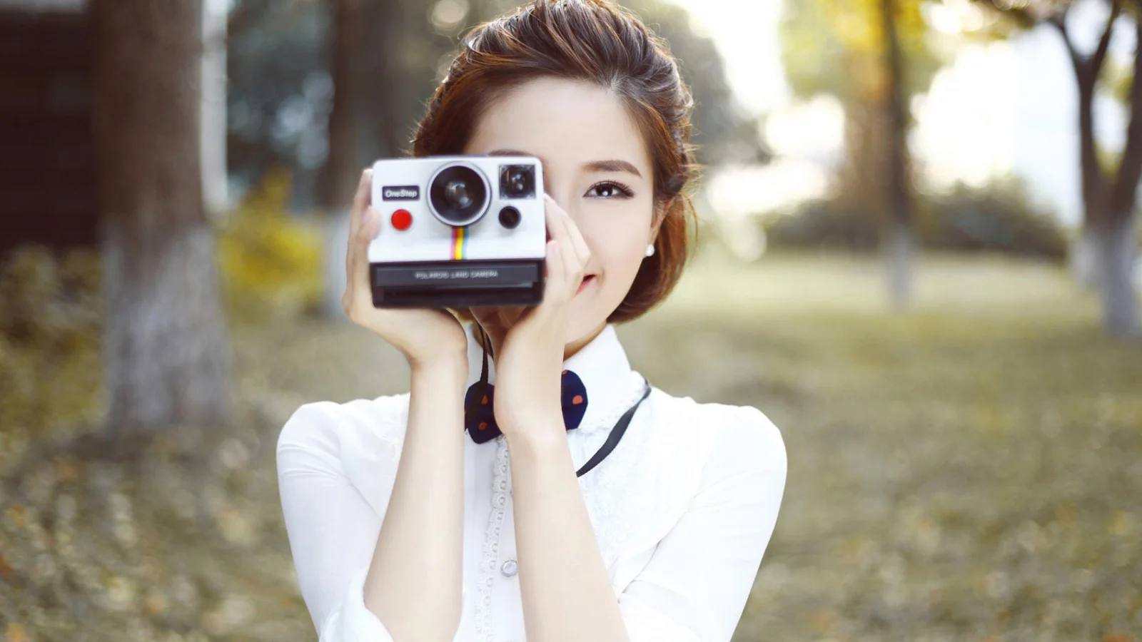 야외 공원에서 한 여성이 즉석카메라를 들고 사진을 찍고 있다.