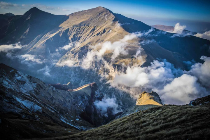 高山山脊与深邃山谷被翻涌的云雾环绕，天空呈现明亮的蓝色。