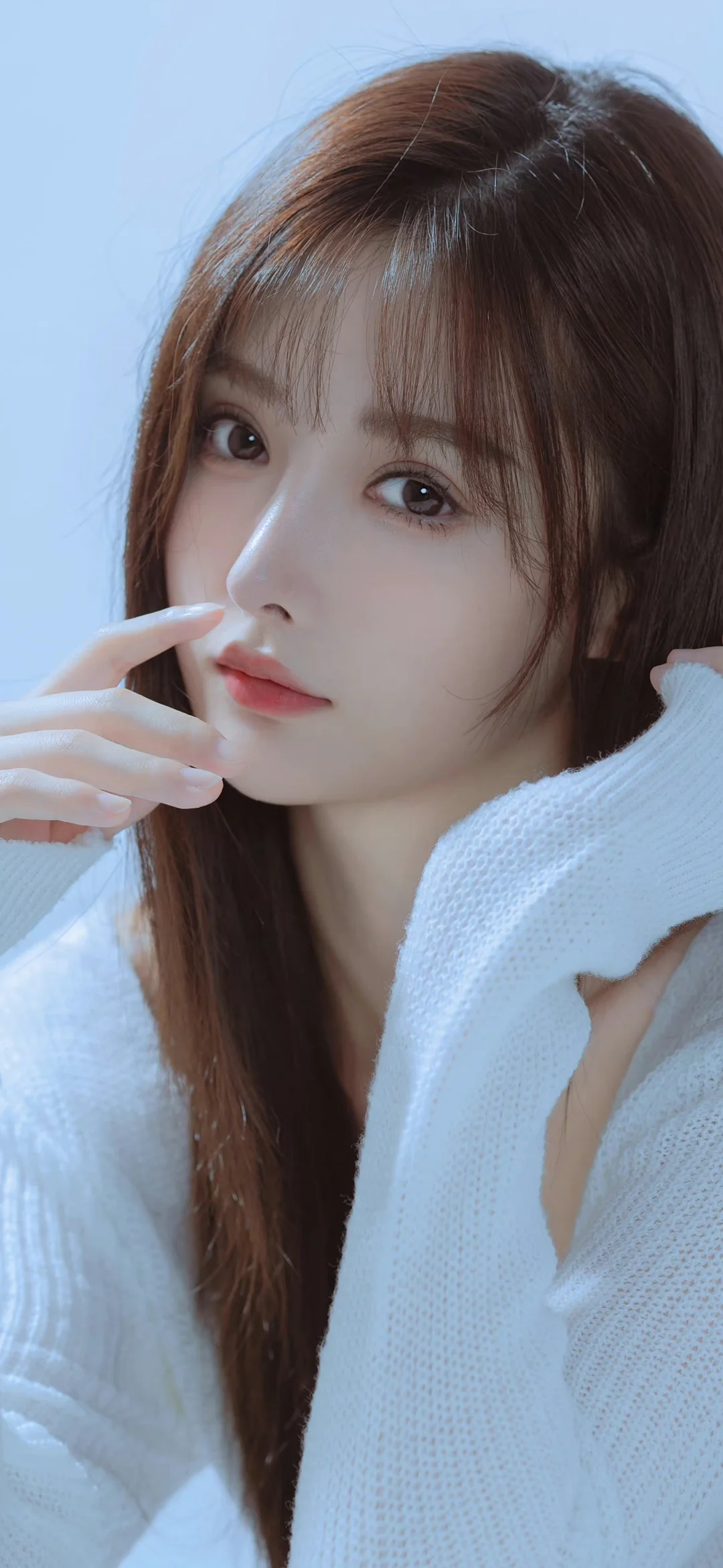 一名棕色长发女子穿着白色针织衫，在浅蓝色背景前进行近距离肖像拍摄。