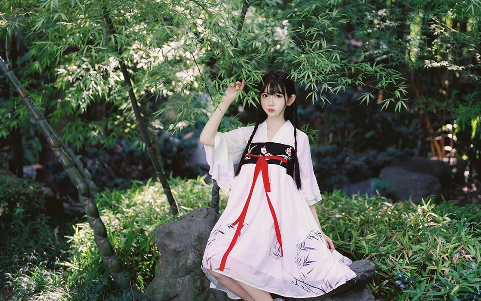 一名身穿淺色漢服的女子坐在竹林中的岩石旁。