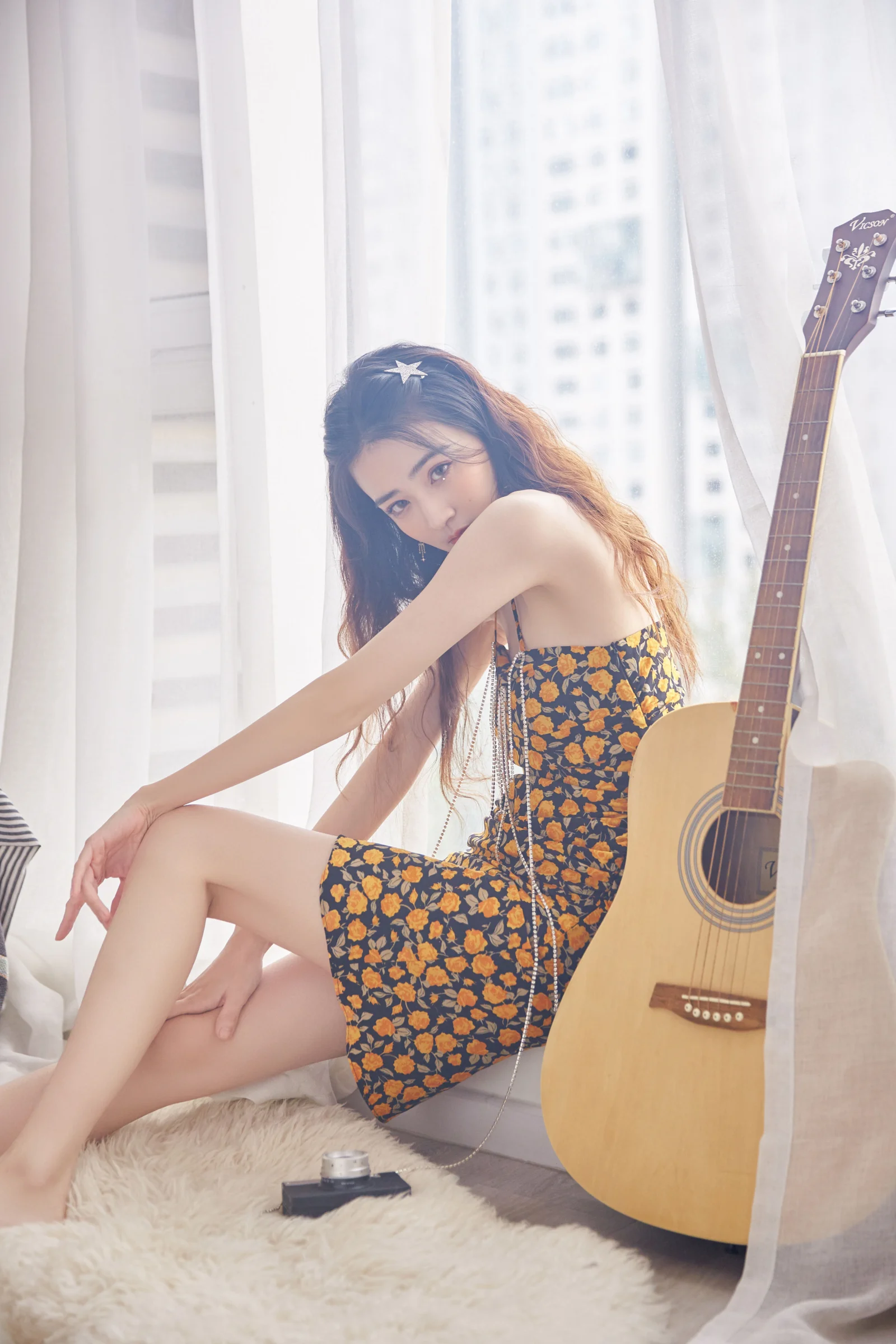 一名穿花卉图案连衣裙的女性坐在窗边，身旁放着一把木质原声吉他。