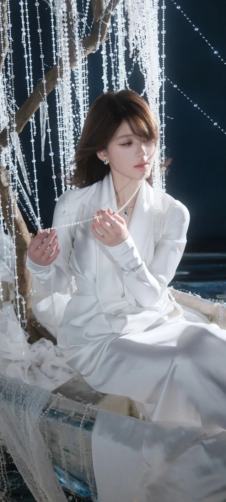一名成年女性身穿白色连衣裙坐在串珠帘幕前。